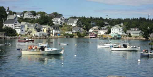 A serene harbor scene with boats anchored in calm water, surrounded by colorful houses and lush greenery.