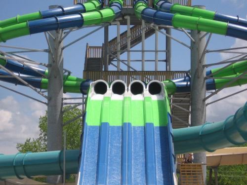 A colorful water slide structure with multiple twisting tubes and a staircase in a sunny outdoor setting.