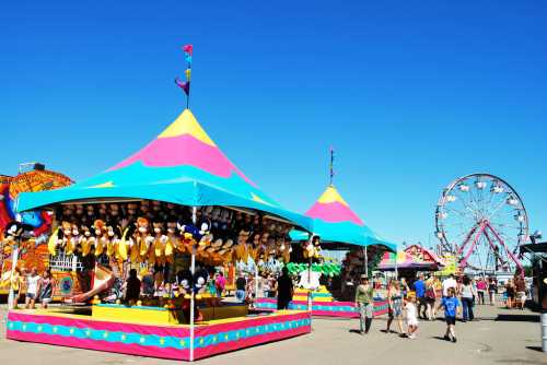 Colorful carnival tents with games and prizes, a Ferris wheel in the background, and people enjoying the festivities.