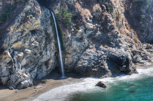A serene coastal scene featuring a waterfall cascading down rocky cliffs into a tranquil ocean.