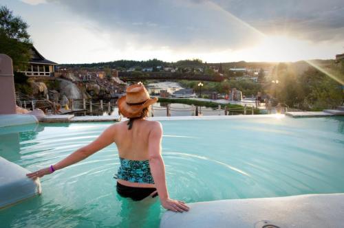 A person in a swimsuit and hat relaxes in a pool, overlooking a scenic sunset and landscape.
