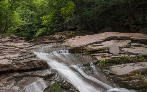 A serene waterfall cascading over smooth rocks, surrounded by lush green trees in a tranquil forest setting.