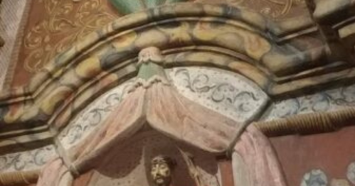 A detailed mural featuring a figure with ornate decorations and a face peeking from beneath a draped fabric.
