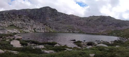 A serene mountain lake surrounded by rocky terrain and lush greenery under a cloudy sky.