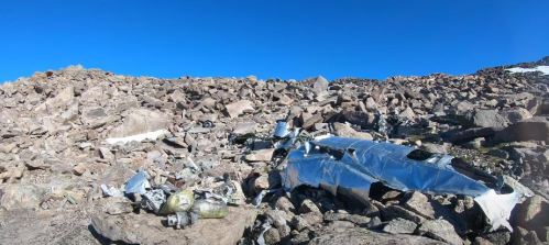 Wreckage of an aircraft scattered among rocky terrain under a clear blue sky.
