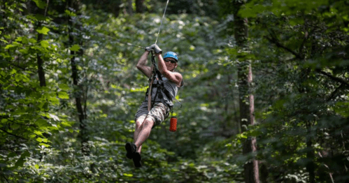 A person zip-lining through a lush green forest, wearing a helmet and gloves, enjoying an outdoor adventure.