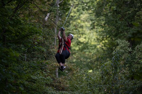 A person in a red shirt zip-lining through a lush green forest, surrounded by trees.