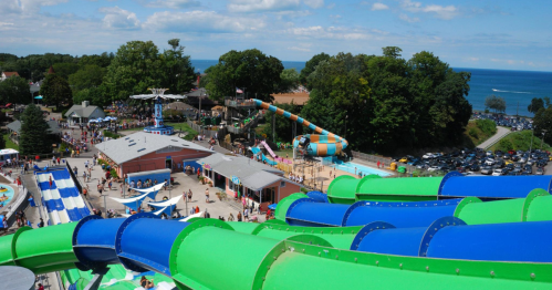 Aerial view of a water park with colorful slides, pools, and a beach in the background on a sunny day.