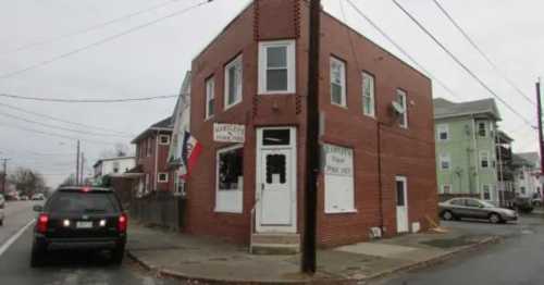 A brick building on a corner lot with a closed storefront, surrounded by residential homes and a parked car.