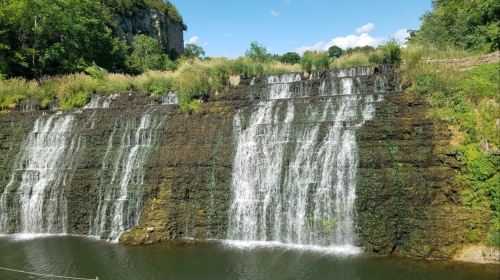 A serene waterfall cascading over a rocky cliff, surrounded by lush greenery and a clear blue sky.