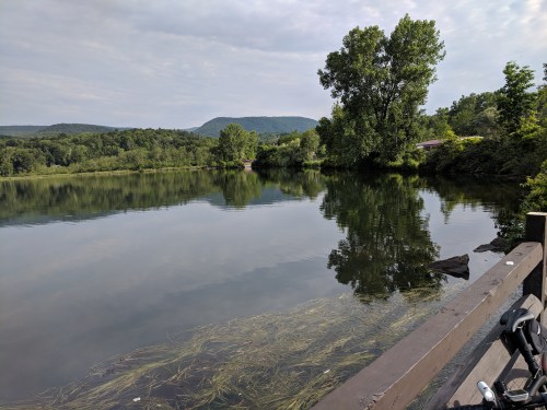 A serene lake surrounded by lush greenery and distant hills, reflecting the sky and trees in calm waters.