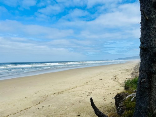 A serene beach scene with gentle waves, soft sand, and a cloudy blue sky in the background.