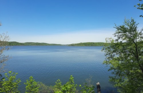 A serene lake surrounded by lush green hills under a clear blue sky.