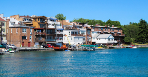 Colorful buildings line a waterfront, with boats docked and trees in the background under a clear blue sky.