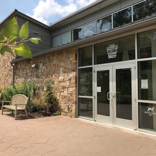 Exterior view of a stone building with large windows, a bench, and a sign for the Department of Conservation and Natural Resources.