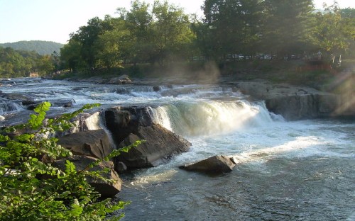 A serene waterfall cascades over rocks, surrounded by lush greenery and mist in a tranquil natural setting.