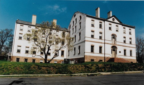 Historic white brick buildings with a tree in front, set against a clear blue sky.