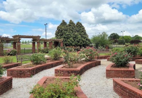A landscaped garden with brick pathways, rose bushes, and a pergola under a partly cloudy sky.