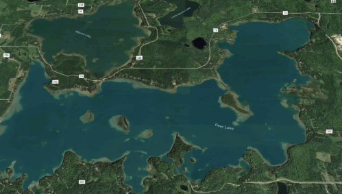 Aerial view of a large, blue lake surrounded by green forests and winding roads.