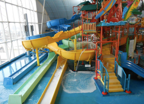 Colorful water slides and play structures in an indoor water park, with a blue pool and bright decor.