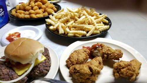 A spread of food including a burger, fried chicken, fries, and cheese balls on plates.