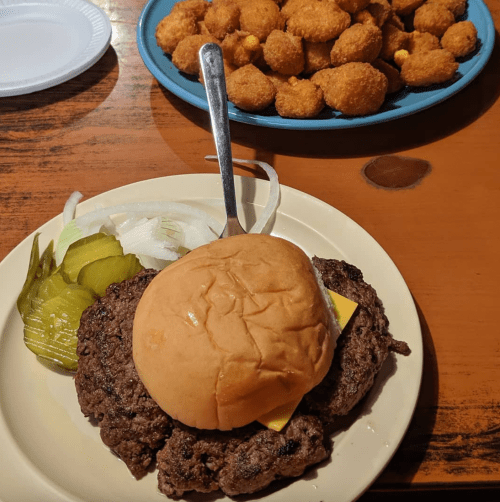 A plate with a cheeseburger, pickles, and onions, alongside a bowl of golden fried snacks.