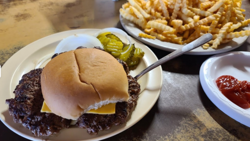 A plate with a cheeseburger, pickles, and a side of crinkle-cut fries with ketchup on the side.