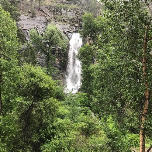 A cascading waterfall surrounded by lush green trees and rocky cliffs in a serene natural setting.