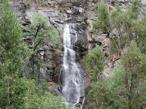 A cascading waterfall flows down rocky cliffs, surrounded by lush green trees and foliage.