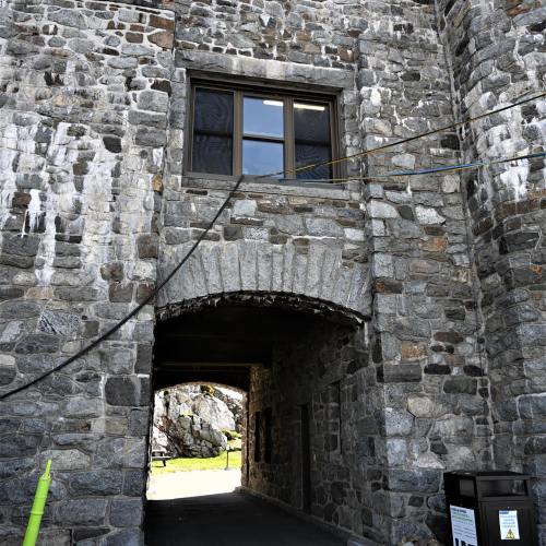 Stone archway leading to a passageway, with a window above and textured stone walls.