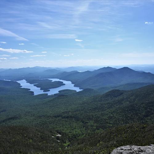 A panoramic view of lush green mountains and a winding lake under a clear blue sky.