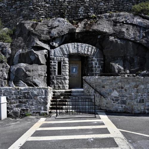 Stone entrance to a building set into a rocky hillside, with steps leading up and a barrier in front.