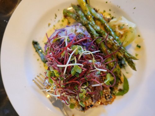 A plated dish featuring grilled asparagus, cabbage, and a colorful topping of sprouts and shredded vegetables.