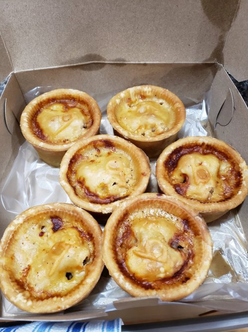 A box containing six golden-brown custard tarts with a flaky crust.