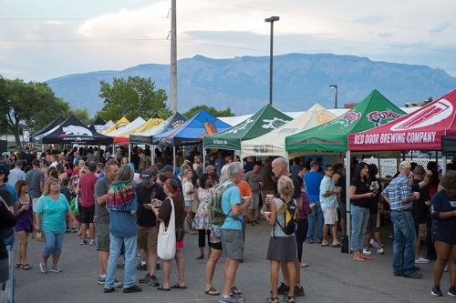 A lively outdoor event with crowds enjoying various tents and booths, set against a backdrop of mountains.