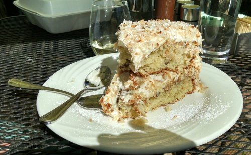 A slice of layered cake topped with frosting and coconut, served on a white plate with two spoons.