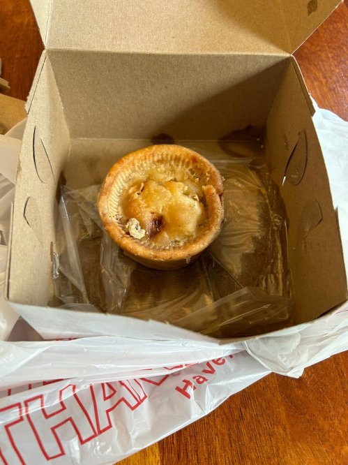 An empty takeout box with a single, partially eaten dessert pie inside, resting on a plastic bag.