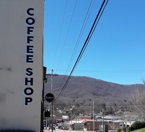 A coffee shop sign on a building with a clear blue sky and mountains in the background. Power lines crisscross the scene.