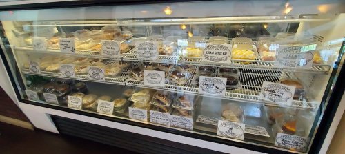 A display case filled with various baked goods, each labeled with names and prices.