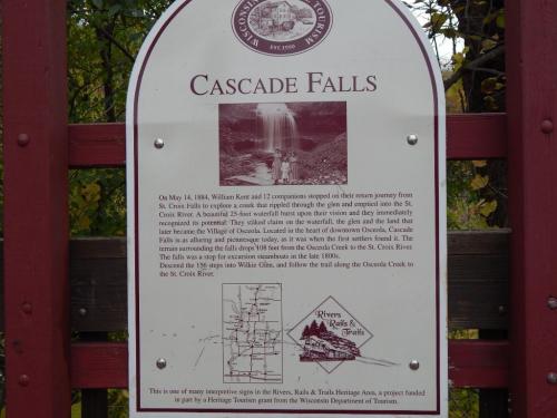 Sign about Cascade Falls, detailing its history and significance, with a waterfall visible in the background.
