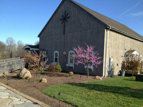 A rustic wooden barn with a star decoration, surrounded by blooming trees and landscaped gardens under a clear blue sky.