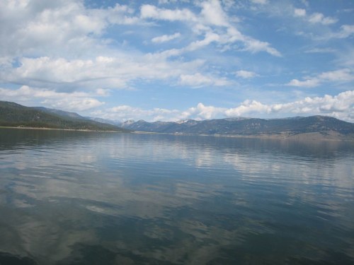 A serene lake reflecting mountains and a blue sky with fluffy clouds, creating a peaceful natural landscape.