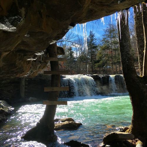 A serene waterfall cascades into a turquoise pool, framed by rocky cliffs and icicles hanging from above.