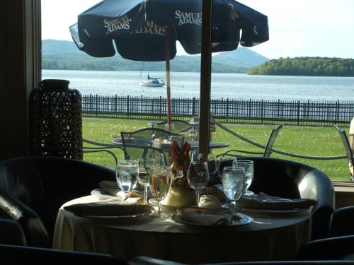 A dining table set with glasses and a centerpiece, overlooking a lake and mountains through a large window.