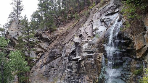 A waterfall cascading down rocky cliffs, surrounded by trees and rugged terrain.