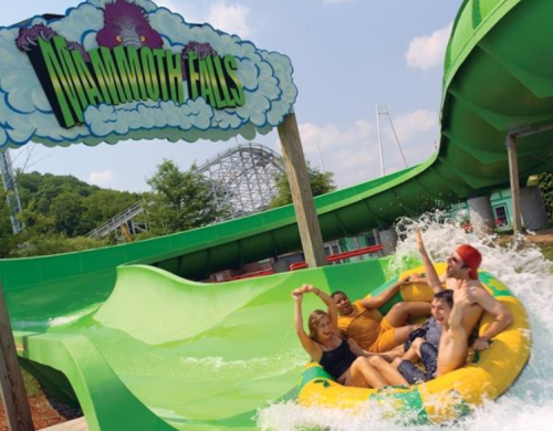 Four friends enjoy a water slide ride at Mammoth Falls, splashing through water with excitement on a sunny day.