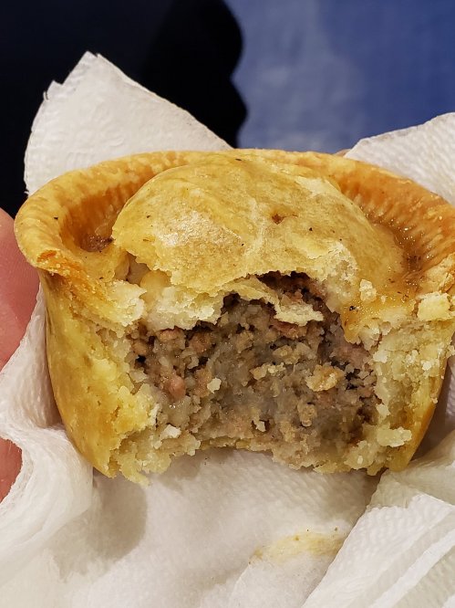 A hand holding a partially eaten meat pie on a napkin, revealing a savory filling inside.