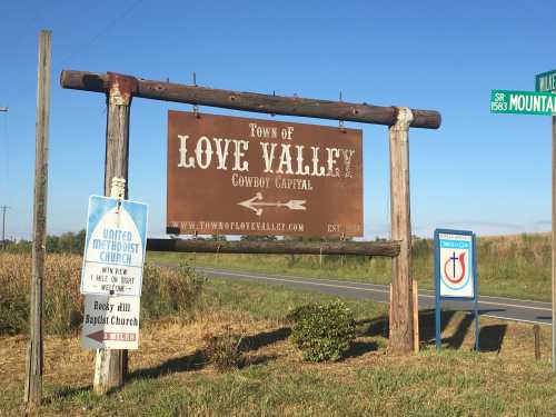 Sign for Love Valley, Cowboy Capital, with directions to local churches and a road sign in the background.