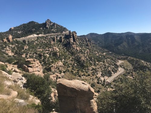A scenic view of rocky mountains and winding roads under a clear blue sky.