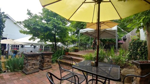 A cozy outdoor patio with yellow umbrellas, stone planters, and lush greenery, inviting for relaxation and dining.